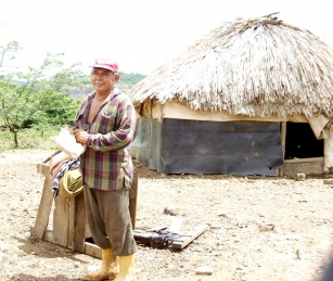 Prosendo Fernandez stands in front of a mud hut fortified with plastic tarps from the mine's dump.