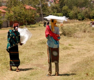 Two women carry home mosquito nets they purchased for $1 each in their village of Engutoto, Tanzania.