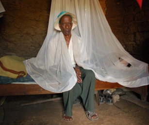Malaria patient Elsante Karangira Pallangya sits with his mosquito net, which is riddled with holes. Pallangya must share two bed nets with his family of five in the village of Patandi, Tanzania.