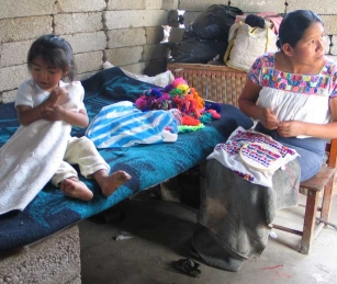 Virginia Bocato de la Pila embroiders while her daughter Mariel plays. She sells blouses, usually one a month.